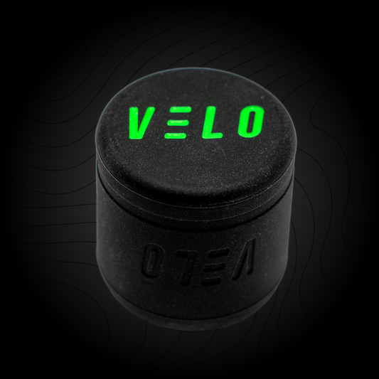 A black VELO baseball puck knob attachment with the brand name 'VELO' written in green on the bottom surface.