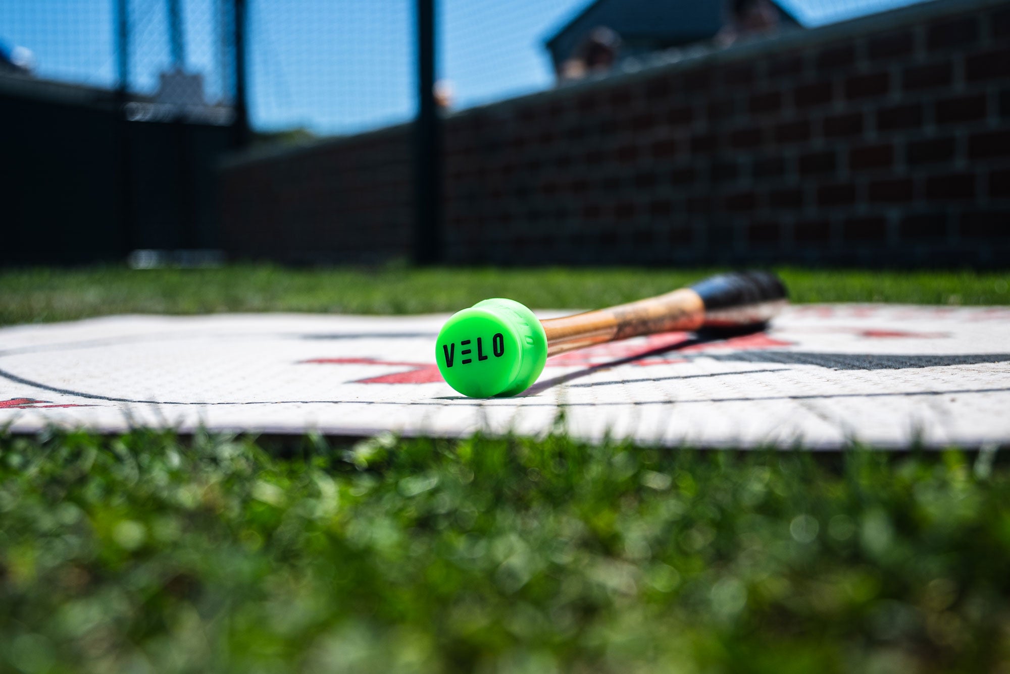 Baseball bat laying on On-Deck circle at Cape Cod League game with attached green VELO Puck