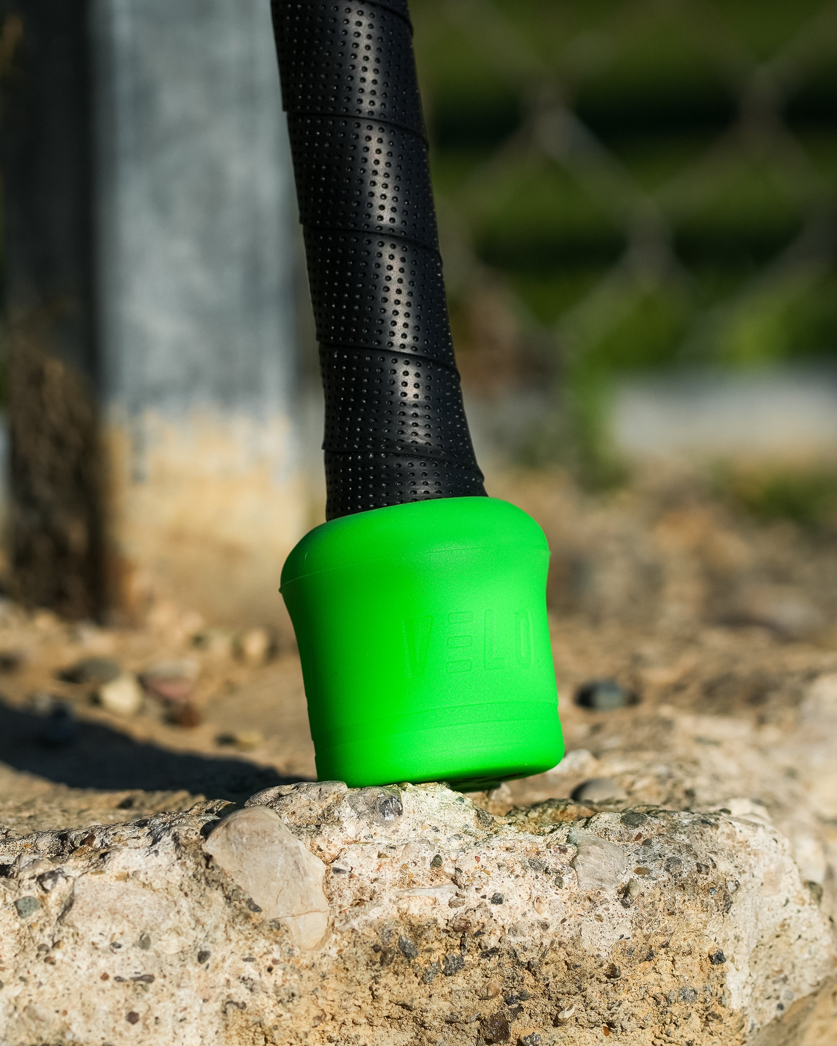 VELO Overspeed bat resting against bench with small green VELO Puck